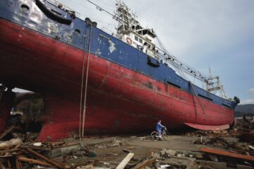 KESSENNUMA, JAPAN - MARCH 29: A made rides past a ship that was washed ashore and debris scatter around Shinhamacyo area after a massive earthquake and tsunami hit northern Japan March 29, 2011 in Kesennuma, Miyagi, Japan. More than 10,000 were killed and more than 17,000 are still missing by the disaster hit on March 11.