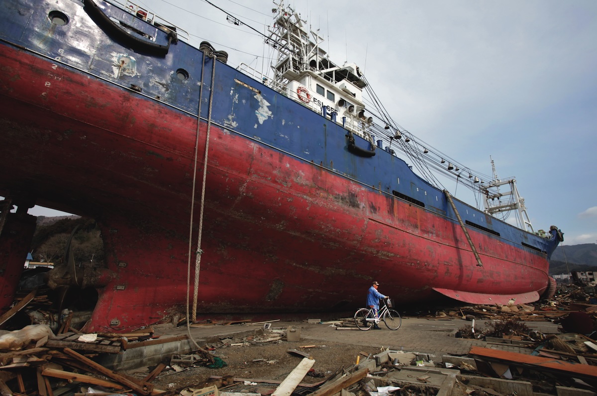 KESSENNUMA, JAPAN - MARCH 29: A made rides past a ship that was washed ashore and debris scatter around Shinhamacyo area after a massive earthquake and tsunami hit northern Japan March 29, 2011 in Kesennuma, Miyagi, Japan. More than 10,000 were killed and more than 17,000 are still missing by the disaster hit on March 11.