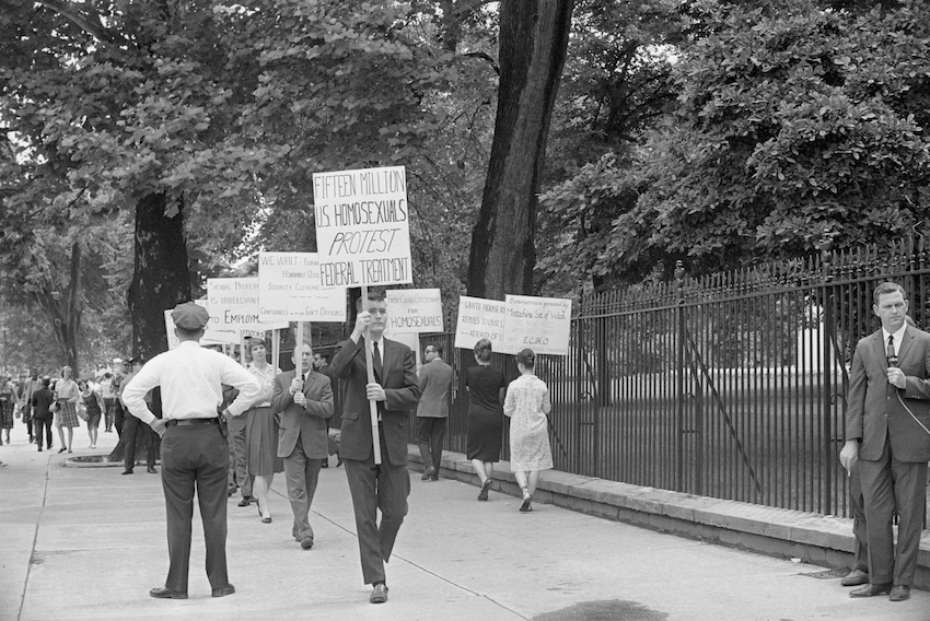 Black and white image of a man walking down the street holding a protest sign.