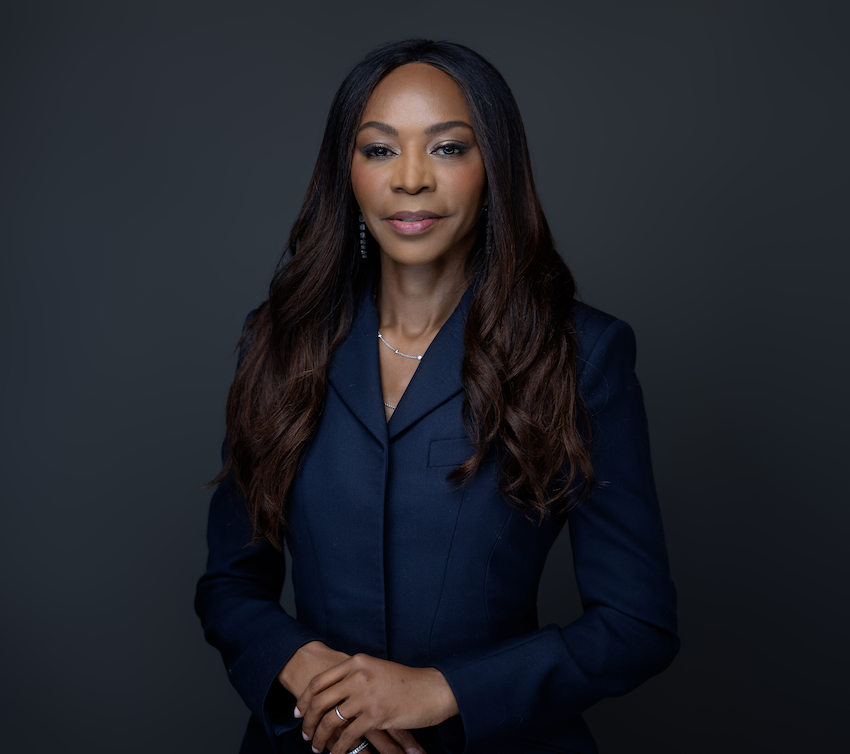 A portrait of global economist Dambisa Moyo in a navy suit in front of a dark gray backdrop.