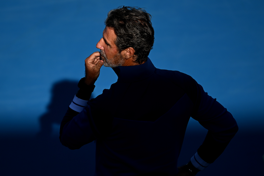 Side profile of tennis couch Patrick Mouratoglou looking off to the side on a blue tennis court.