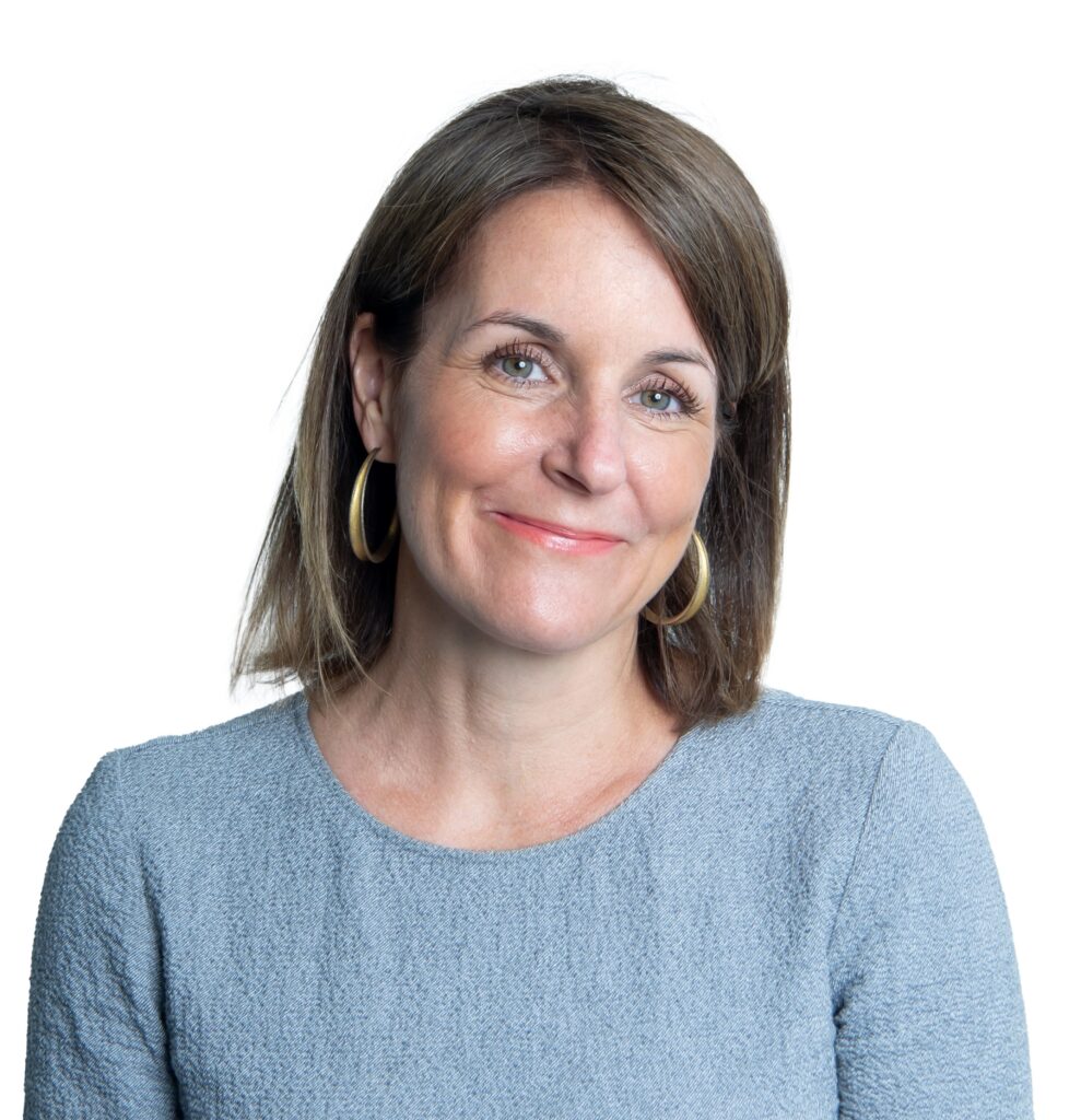 A portrait of a smiling woman wearing a light blue shirt and peach lipstick