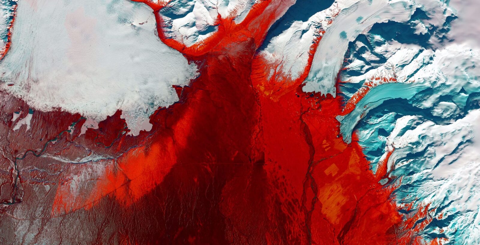 A striking satellite image showing a dramatic contrast between red land masses and ice-blue glaciers or snow-covered terrain. The red areas depict land or possibly vegetation using false-color infrared imaging, while the white and blue regions represent ice, snow, and water. The image highlights the patterns and textures of Earth's surface in a polar or high-latitude region.