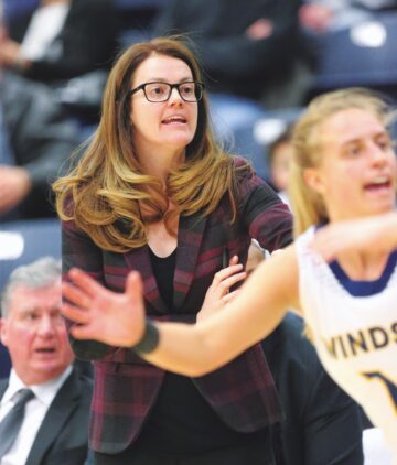 a woman coach on the sidelines speaking to her female players as they are playing basketball.