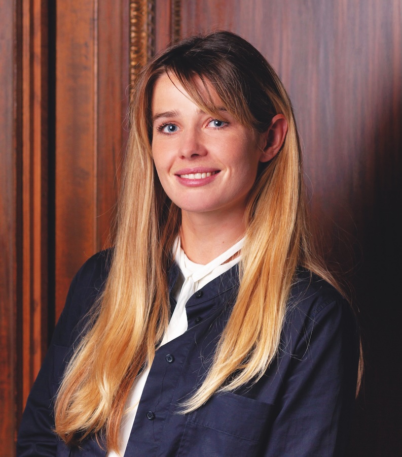 Headshot of Lucy Orr-Ewing in a navy top standing in front of a rich wooden wall