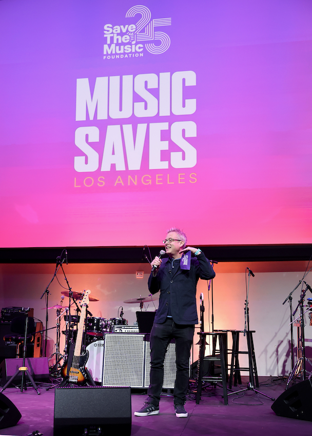 Executive Director Henry Donahue speaks during Save The Music’s 2023 25 Years Celebration at NeueHouse Hollywood in front of a pink & purple gradient screen that portrays the events logo.