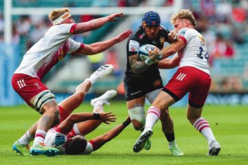 An image of 4 men playing rugby, one is on the ground and 3 others pushing each other.