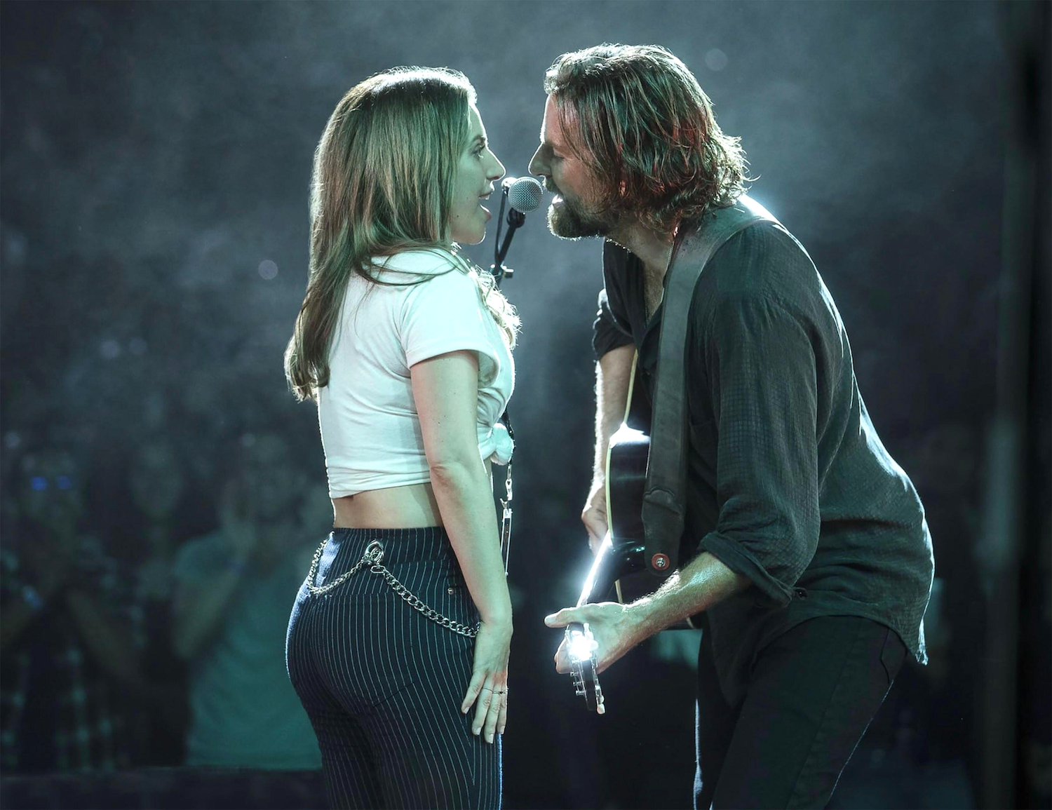 a still from the movie A Star is Born from 2018, Lady Gaga and Bradley Cooper sing together sharing the same microphone on stage