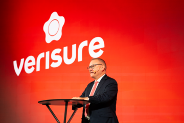 a man standing at a podium on a stage in front of a bright red background with the word Verisure on it.