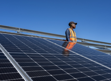 A worker in an orange safety vest standing behind a very large solar panel to install it
