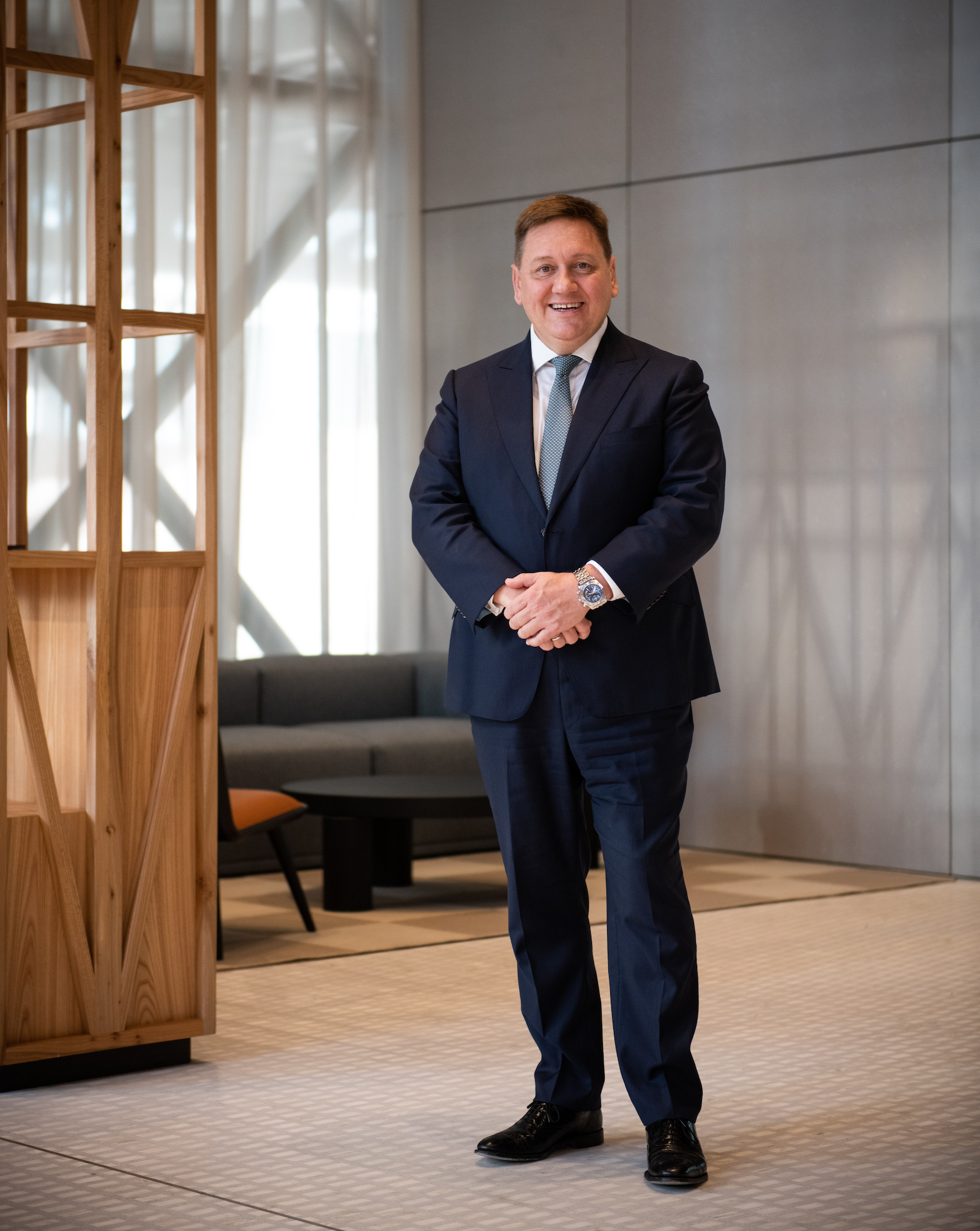 a photograph of a man in a navy suit standing in a large open room smiling at the camera
