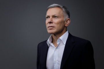 a photograph of a man in a navy suit and white button down looking off into the distance.