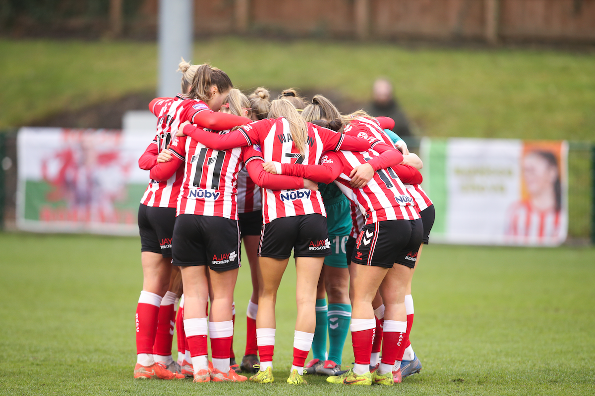 a photograph of a group of female athletes in red and white striped jerseys huddled together on a grass field.