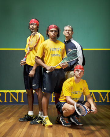a photographic portrait of three squash players in yellow jerseys and protective eyewear standing along with an older gentleman in a green track suit