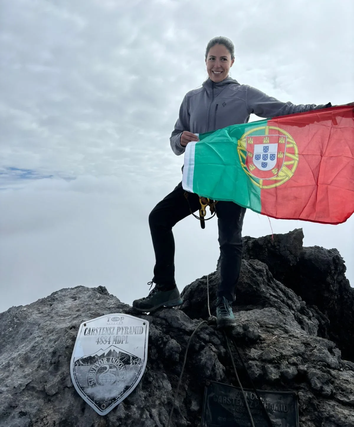 a photo of a woman standing on top of a mountain holding a flag.