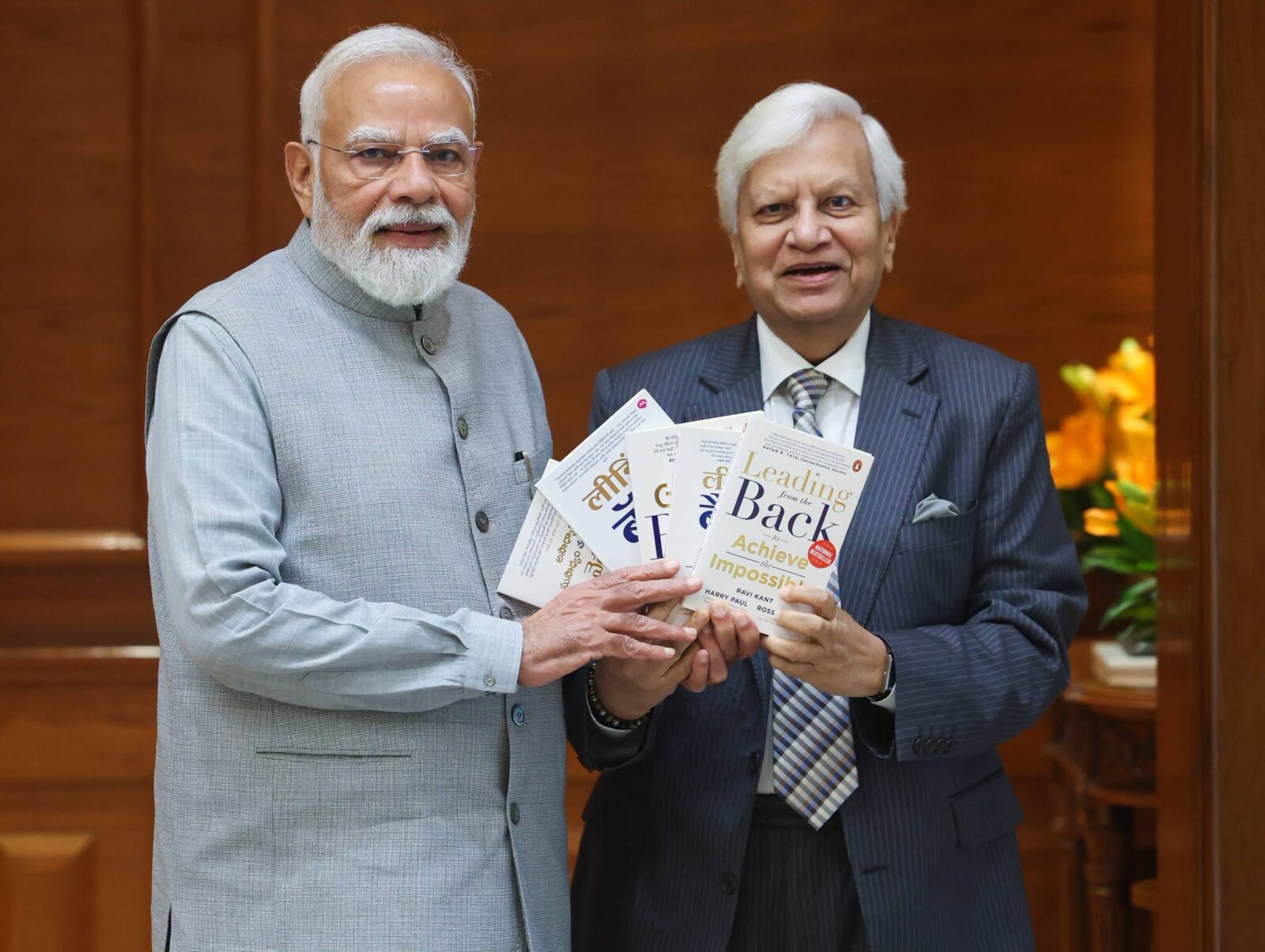 A photograph of two men with white hair smiling for the camera both holding several copies of the same book