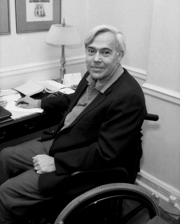 a black and white photograph of an older man in a wheelchair sitting at a desk